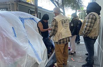 People in ERT (Encampment Resolution team) uniform around a guy near homeless shelter